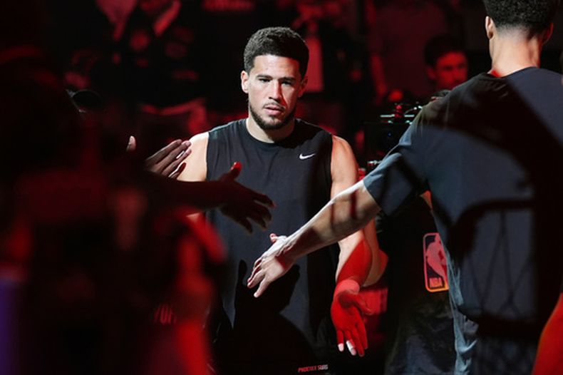 ARCHIVO - Devin Booker, de los Suns de Phoenix, saluda a sus compañeros de equipo durante la presentación previa al tercer juego de la serie de primera ronda de los playoffs del baloncesto de la NBA contra el Thunder de Oklahoma City, el 25 de abril de 2026, en Phoenix. (AP Foto/Ross D. Franklin, Archivo)