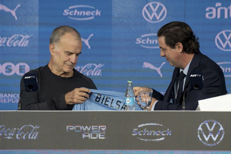 El presidente de la Asociación Uruguaya de Fútbol, Ignacio Alonso (derecha), le entrega la camiseta de la selección al nuevo técnico Marcelo Bielsa durante una rueda de prensa, el miércoles 17 de mayo de 2023, en Montevideo. (AP Foto/Santiago Mazzarovich)