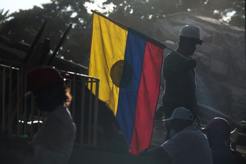 Un bombero que trabaja en las labores de búsqueda y rescate sostiene una bandera de Colombia en medio de los escombros, el jueves 13 de agosto de 2026, tres días después de que un sismo Cali, Colombia. (AP Foto/Iván Valencia)