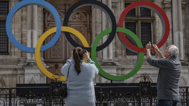 ARCHIVO - Dos personas toman fotos de los anillos olímpicos en el ayuntamiento de París, el 30 de abril de 2023. (AP Foto/Aurelien Morissard)