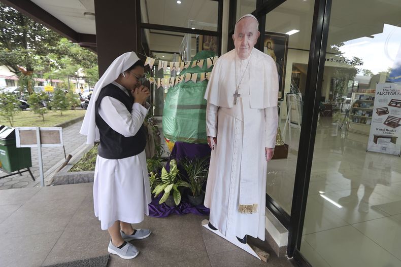 Una monja católica reza frente a una imagen de cuerpo entero del papa Francisco en Yogyakarta, Indonesia, el lunes 21 de abril de 2025. (AP Foto/Slamet Riyadi)