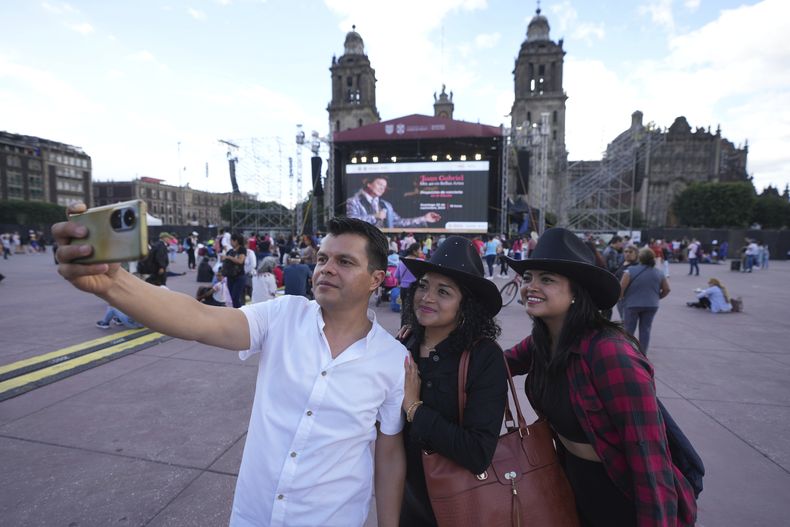 Manuel Torres se toma una selfie con su esposa Ana Ordaz, centro, y su hija Paola Torres previo a una proyección de un concierto de Juan Gabriel en el Zócalo, la plaza principal de la Ciudad de México, el domingo 22 de septiembre de 2024. (Foto AP/Fernando Llano)