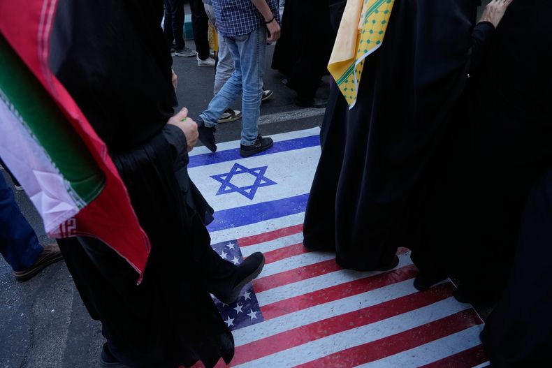 Manifestantes caminan sobre una representación de las banderas de EEUU e Israel durante una manifestación en Teherán, el martes 4 de noviembre de 2025. (AP Foto/Vahid Salemi)