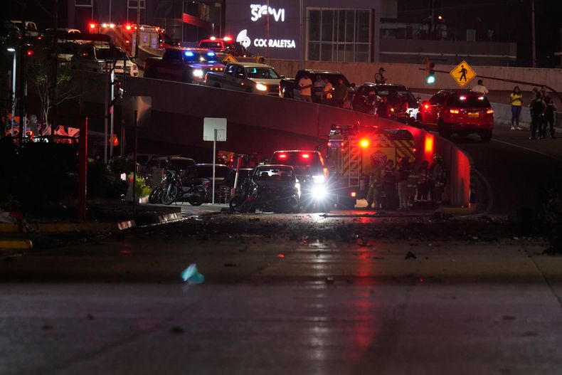 Policías, bomberos y agentes de seguridad inspeccionan los daños en el lugar de la explosión de un automóvil en una calle comercial de Guayaquil, Ecuador, el martes 14 de octubre de 2025. (Foto AP/César Muñoz)