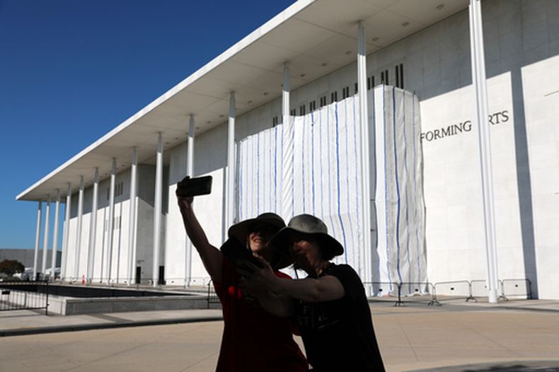 Dos mujeres se toman una selfie con el muro del John F. Kennedy Center for the Performing Arts cubierto por una lona mientras continúan los trabajos para retirar el nombre del presidente Donald Trump, el sábado 13 de junio de 2026, en Washington. (AP Foto/Rahmat Gul)
