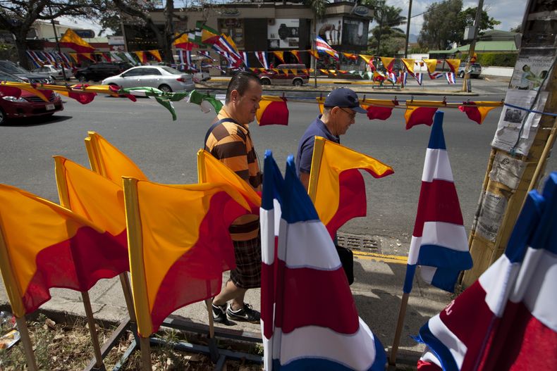 Dos hombres caminan frente a banderas de Costa Rica y de partidos pol&iacute;ticos en San Jos&eacute;, el s&aacute;bado 5 de abril de 2014. Costa Rica vota el domingo en segunda vuelta de las elecciones presidenciales, para elegir entre el opositor Luis G