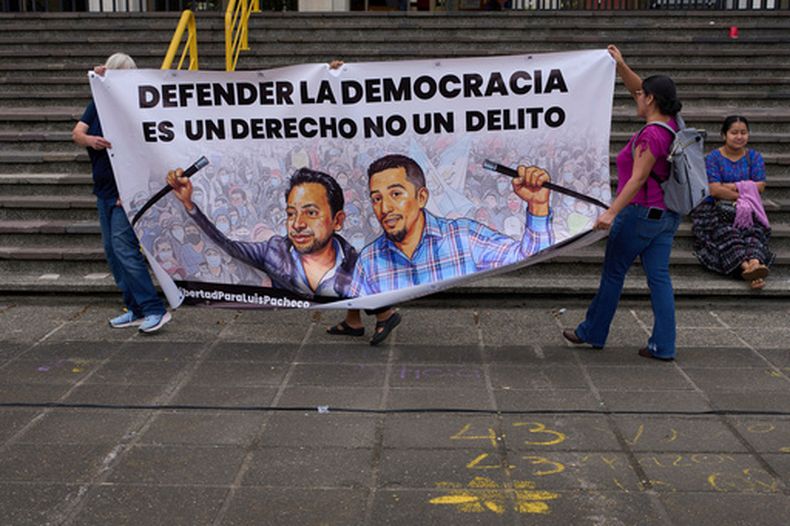 ARCHIVO - Activistas portan una pancarta que dice Defender la democracia es un derecho no un delito sobre retratos de los líderes indígenas encarcelados Luis Pacheco (izquierda) y Héctor Chaclán, quienes enfrentan cargos de terrorismo y asociación ilícita en relación con las protestas nacionales de 2023, frente a la Corte Suprema en Ciudad de Guatemala, el 25 de agosto de 2025. (Foto AP/Moisés Castillo, Archivo)