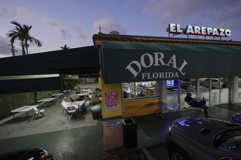 Ciudadanos estadounidenses que inmigraron de Venezuela hace entre 16 y 30 años juegan al dominó fuera de El Arepazo, un restaurante que es un punto de encuentro de la comunidad venezolana en Estados Unidos, en Doral, Florida, el miércoles 2 de abril de 2025. Muchos de los amigos, como César Mena, a la derecha, votaron por el presidente Donald Trump y le siguen apoyando. Mena dijo que tenía familiares y amigos amparados por el TPS, y lo lamentaba por ellos, pero era una situación temporal y había un problema que resolver. (AP Foto/Rebecca Blackwell)