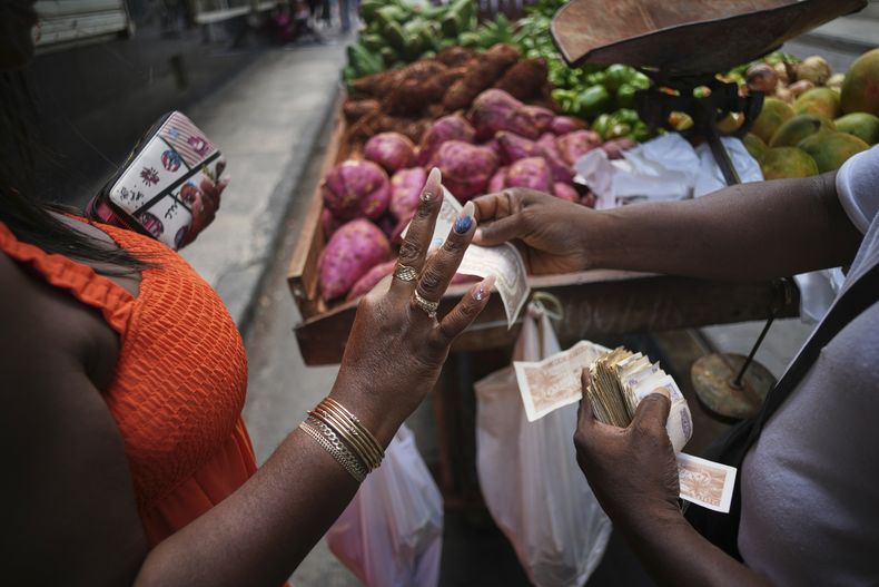 Maite Hernandez, que luce sus uñas arregladas, toma el cambio de un vendedor de verduras en La Habana, Cuba, el sábado 5 de julio de 2025. (AP Foto/Ramon Espinosa)