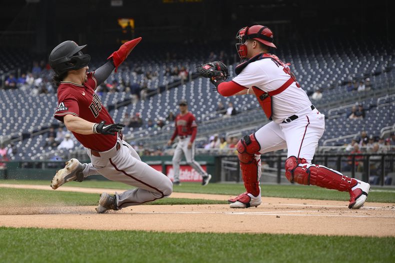 Corbin Carroll de los Diamondbacks de Arizona anota una carrera ante el receptor Riley Adams de los Nacionales de Washington, el jueves 22 de junio de 2023. (AP Foto/Nick Wass)