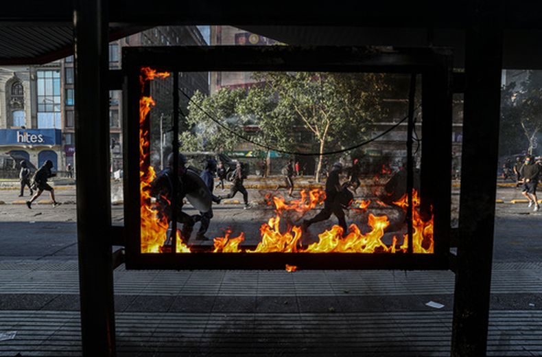 ARCHIVO - Unos manifestantes corren junto a una parada de autobús en llamas mientras buscan refugio de la policía durante los enfrentamientos que se produjeron tras una manifestación contra el presidente Sebastián Piñera en la que se exigía la liberación de los manifestantes antigubernamentales detenidos desde que comenzaron las protestas antigubernamentales en 2019, en Santiago de Chile, el 27 de noviembre de 2020. (Foto AP/Esteban Félix, archivo).