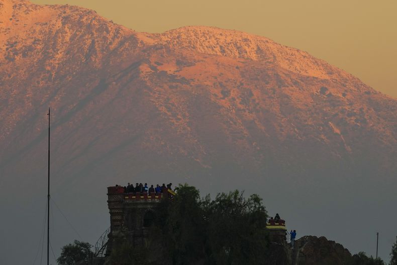 ARCHIVO - El sol del atardecer ilumina Los Andes con una capa de nieve mientras visitantes toman fotos desde Santa Lucía, en Santiago, Chile, el 8 de mayo de 2024. (AP Foto/Esteban Félix, Archivo)