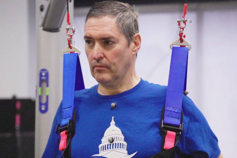 Esta imagen de video facilitada por el Centro Médico de la Universidad de Pittsburgh (UPMC) y la Escuela de ciencias de la salud de la Universidad de Pittsburgh muestra a Doug McCullough, que padece atrofia muscular espinal, durante las pruebas de estimulación experimental de la médula espinal para mejorar la función muscular en Pittsburgh, el 14 de marzo de 2023. (UPMC, University of Pittsburgh Health Sciences via AP)