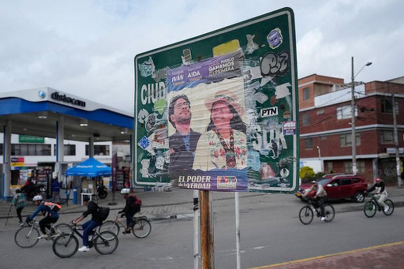 Ciclistas circulan detrás de un cartel de campaña del senador Iván Cepeda, candidato presidencial de la coalición gobernante Pacto Histórico, antes de las elecciones en Soacha, Colombia, el miércoles 27 de mayo de 2026. (Foto AP/Fernando Vergara)