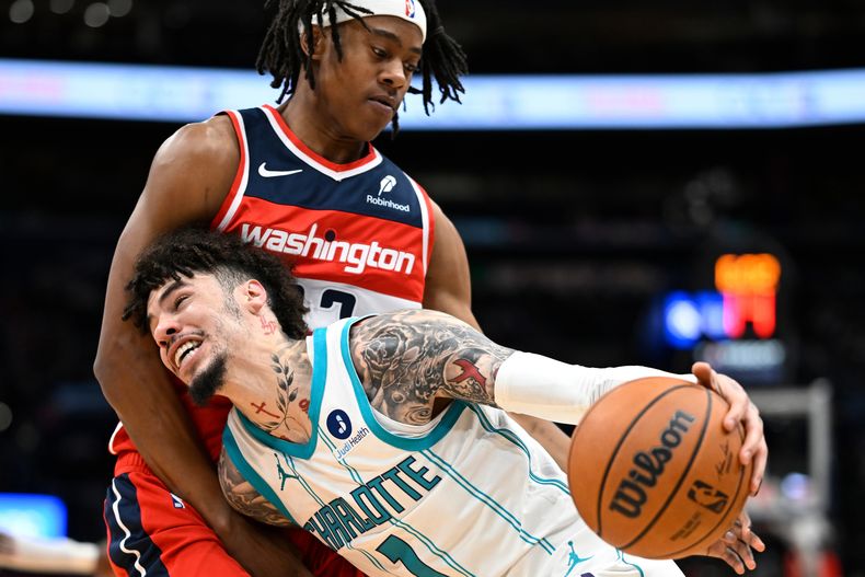 LaMelo Ball (1), de los Hornets de Charlotte, lleva el balón frente a Tre Johnson, arriba, de los Wizards de Washington, durante la primera mitad del partido de baloncesto de la NBA, el domingo 26 de octubre de 2025, en Washington. (AP Foto/John McDonnell)
