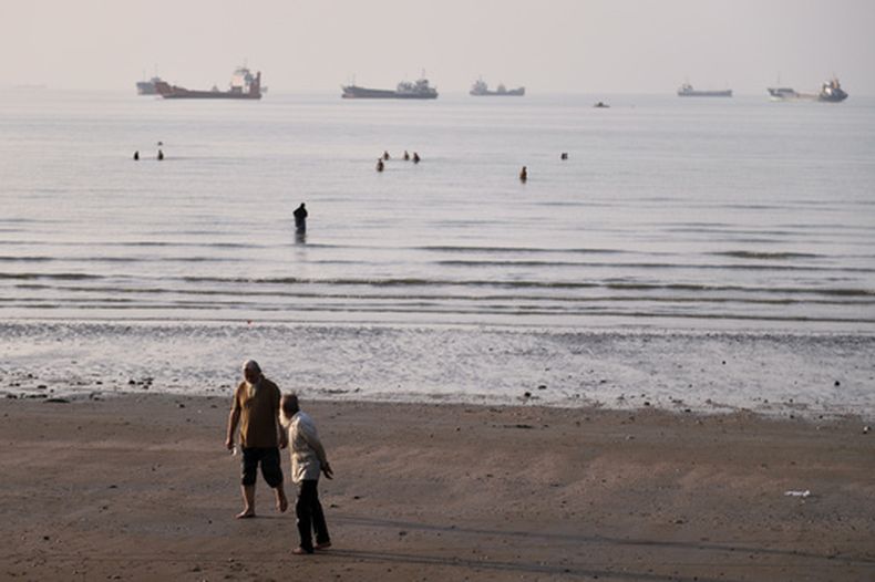 Personas caminan por la playa mientras otras se adentran en el agua en el estrecho de Ormuz, donde buques de carga y de servicio se encuentran anclados frente a Bandar Abbas, Irán, el lunes 1 de junio de 2026. (Amirhosein Khorgooi/ISNA vía AP)