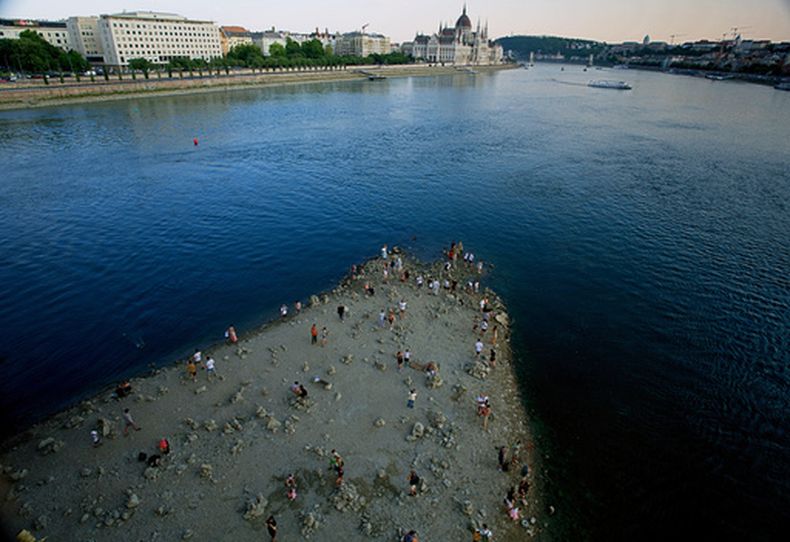 Personas caminan sobre un banco de arena bajo el Puente Margareth del río Danubio, el miércoles 5 de agosto de 2026, en el centro de Budapest. (AP Foto/Bela Szandelszky)