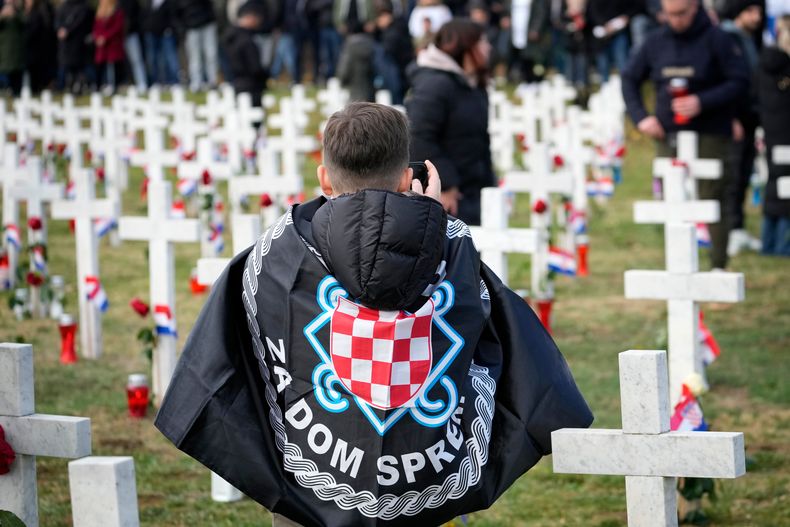 Un joven envuelto en insignias de derechas fotografía el cementerio en el aniversario de la caída de la ciudad de Vukovar, Croacia, durante la guerra de 1991-1995, ante el Ejército yugoslavo liderado por serbios, el 18 de noviembre de 2025. (Foto AP/Darko Bandic)