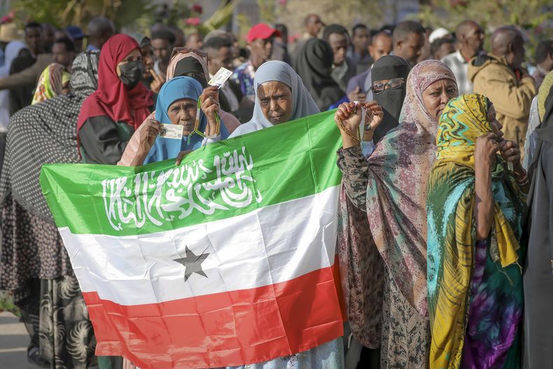 Una mujer muestra la bandera de Somalilandia mientras la gente espera a votar en las elecciones presidenciales de 2024 en un centro electoral en Hargeisa, Somalilandia, el miércoles 13 de noviembre de 2024. (AP Foto/Abdirahman Aleeli)