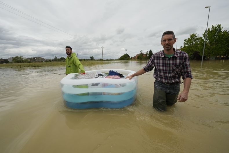 Dos hombres usan una alberca inflable para transportar sus pertenencias en un camino inundado de Lugo, Italia, el jueves 18 de mayo de 2023. (AP Foto/Luca Bruno)