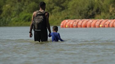 ARCHIVO - Dos migrantes caminan cerca de unas grandes boyas usadas como barrera fronteriza flotante en el Río Grande, o Bravo, el 1 de agosto de 2023, en Eagle Pass, Texas.. (AP Foto/Eric Gay, Archivo)