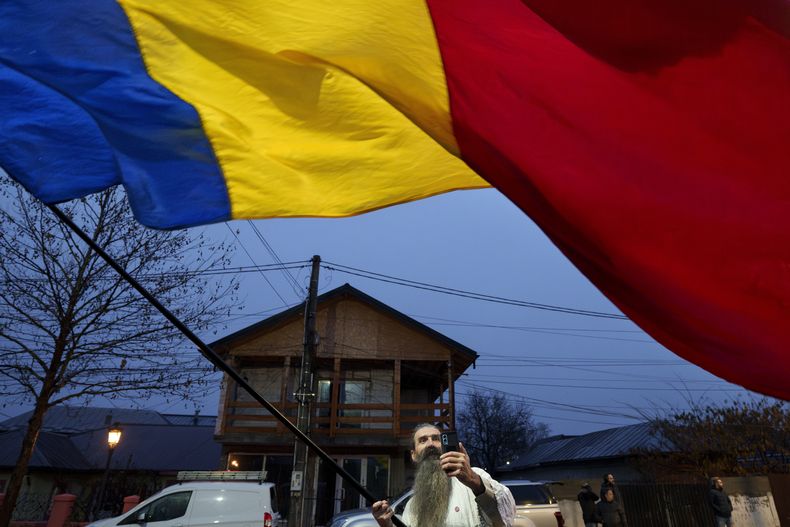 Un hombre ondea la bandera rumana frente al colegio electoral cerrado donde debía votar Calin Georgescu, candidato independiente a la presidencia que ganó la primera vuelta de las elecciones presidenciales, después de que el Tribunal Constitucional de Rumania anulara la primera vuelta de las elecciones presidenciales, en Mogosoaia, Rumania, domingo 8 de diciembre de 2024. (AP foto/Andreea Alexandru)