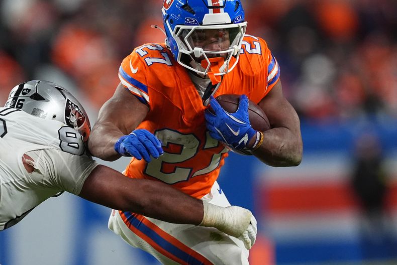 J.K. Dobbins, running back de los Broncos de Denver, a la derecha, corre para un primer down mientras Jonah Laulu, defensive tackle de los Raiders de Las Vegas, realiza la detención en la segunda mitad de un juego de fútbol americano de la NFL el jueves 6 de noviembre de 2025, en Denver. (AP Photo/David Zalubowski)