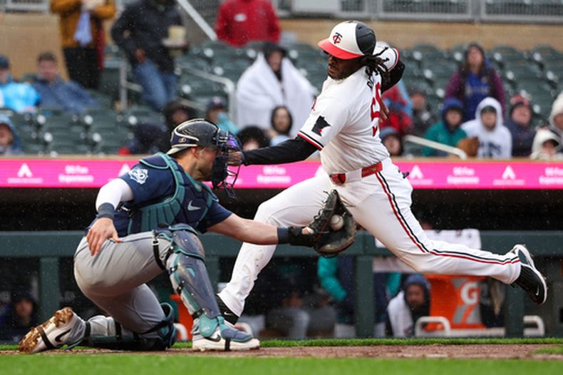 Josh Bell, derecha, bateador designado de los Mellizos de Minnesota, llega a salvo al plato mientras Mitch Garver, izquierda, receptor de los Marineros de Seattle, intenta ponerlo fuera durante la segunda entrada del juego de béisbol de Grandes Ligas, el lunes 27 de abril de 2026, en Minneapolis. (AP Foto/Matt Krohn)