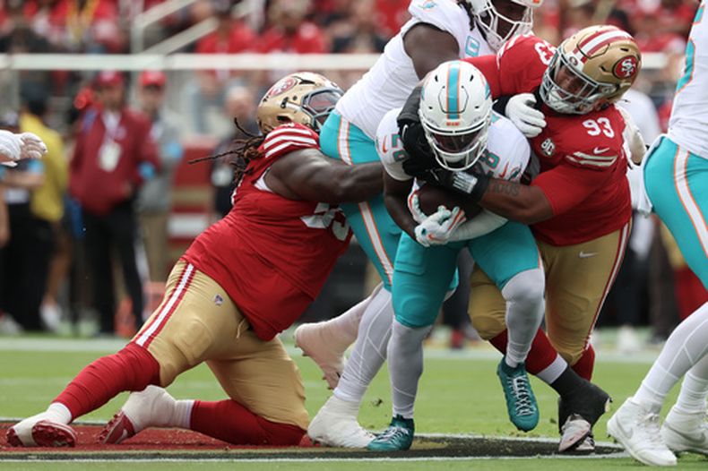 DeVon Achane, al centro, de los Dolphins de Miami, corre mientras CJ West, izquierda, y Gracen Halton (93), tackles defensivos de los 49ers de San Francisco buscan derribarlo durante la primera mitad del partido de la NFL del domingo 20 de septiembre de 2026, en Santa Clara, California. (AP Foto/Jed Jacobsohn)