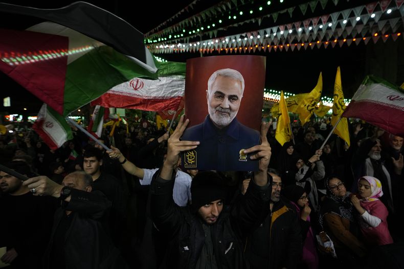 Manifestantes ondean banderas iraníes y palestinas mientras uno de ellos sostiene un cartel con la imagen del fallecido general de la Guardia Revolucionaria iraní Qassem Soleimani, asesinado en un ataque estadounidense en 2020, durante una manifestación contra Israel para condenar la muerte de miembros de la Guardia Revolucionaria en Siria, en la plaza Felestin (Palestina) de Teherán, Irán, el lunes 1 de abril de 2024. (AP Foto/Vahid Salemi)