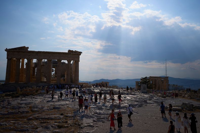 ARCHIVO - Los rayos de sol pasan entre las nubes sobre el antiguo templo del Partenón mientras los turistas pasan por la Acrópolis durante un día caluroso en Atenas, el jueves 2 de julio de 2026. (AP Foto/Petros Giannakouris, Archivo)