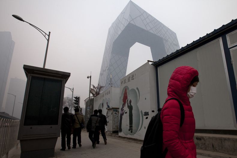 Una mujer cubierta con una mascarilla para frente a un cartel, centro, que proclama "China, adelante", en el distrito comercial central de Beijing el jueves, 20 de febrero del 2014. (Foto AP/Alexander F. Yuan)