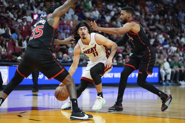 El armador del Heat de Miami Jaime Jaquez Jr. (11) observa para dar un pase entre los defensas de lo Toronto Raptors Malik Williams (35) y Garrett Temple, durante la 1ra mitad del juego de baloncesto de la NBA, el domingo 14 de abril de 2024. (AP Foto/Rebecca Blackwell)