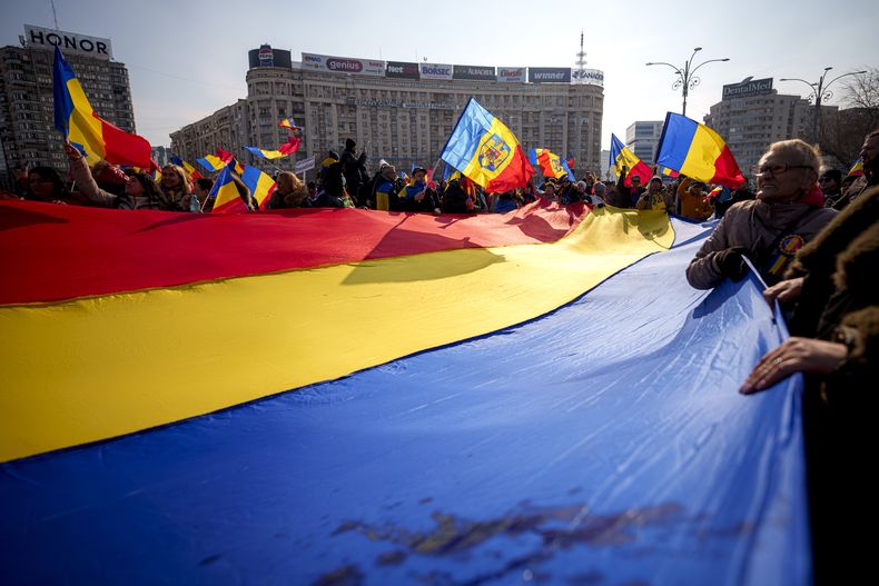 Manifestantes que apoyan a Calin Georgescu, el ganador de la primera vuelta de las elecciones presidenciales rumanas, sostienen una bandera nacional durante una protesta en Bucarest, Rumania, el sábado 22 de febrero de 2025. (AP Foto/Andreea Alexandru)