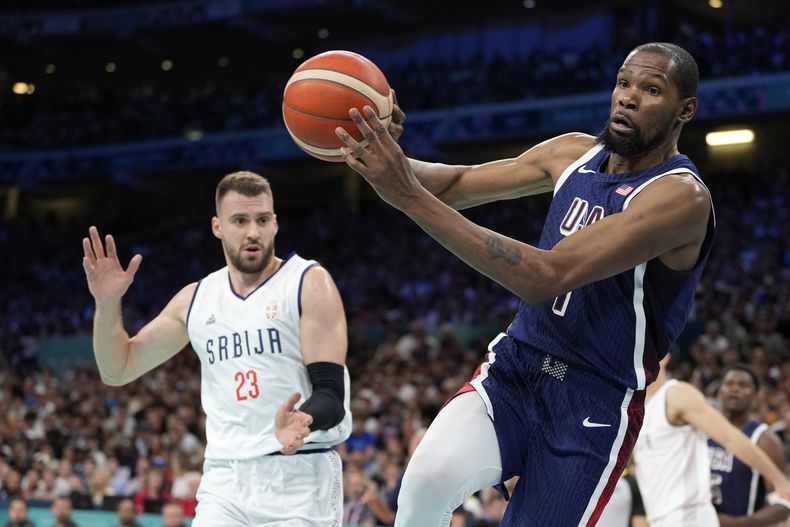 El estadounidense Kevin Durant rescata un balón ante la presión del serbio Marko Guduric durante el partido de la fase de grupos del torneo olímpico de baloncesto, el domingo 28 de julio de 2024, en Villeneuve-dAscq, France. (AP Photo/Michael Conroy)