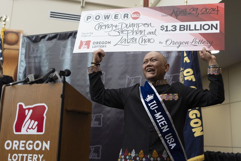 Cheng Charlie Saephan sostiene un cheque gigante por valor de 1.300 millones de dólares sobre su cabeza durante una conferencia de prensa donde se dio a conocer que era uno de los ganadores de la lotería de Powerball, en Salem, Oregon, el lunes 29 de abril de 2024. (AP Foto/Jenny Kane)