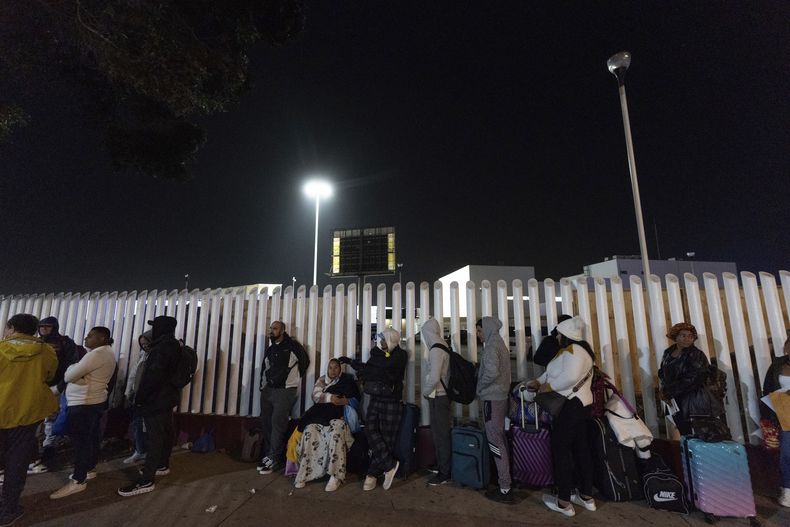 ARCHIVO - Migrantes de Cuba y Venezuela hacen fila en un puesto de control de inmigración mexicano mientras cruzan la frontera para concertar citas para solicitar asilo legalmente en Estados Unidos, el 5 de noviembre de 2024, en Tijuana, México. (AP Foto/Gregory Bull, Archivo)
