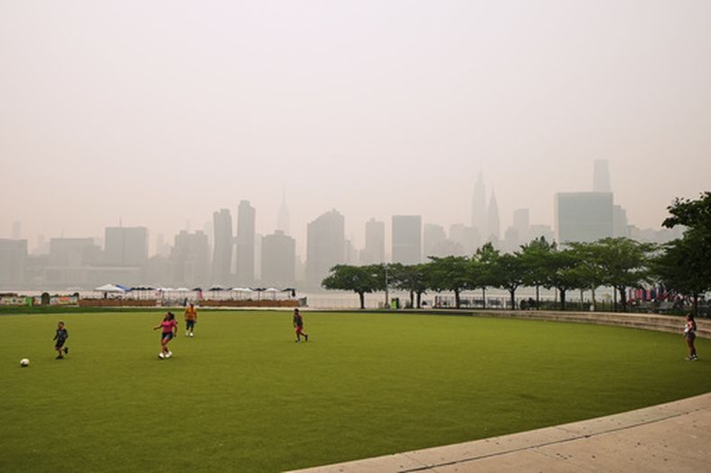 Un grupo de personas juega en el Hunters Point South Park Athletic Field. Al fondo se aprecian los rascacielos de Nueva York, ocultos parcialmente por el humo de los incendios forestales en Canadá, el jueves 16 de julio de 2026 (AP Foto/Frank Franklin II)