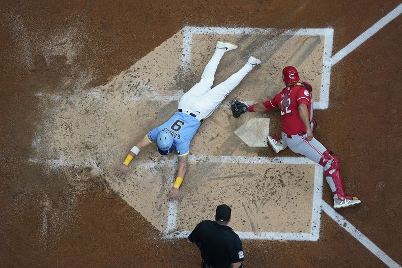 Jake Bauers (9), de los Cerveceros de Milwaukee, se barre a salvo en el plato, superando el toque de Luke Maile, de los Rojos de Cincinnati, durante la segunda entrada del juego de béisbol, el viernes 9 de agosto de 2024, en Milwaukee. (AP Foto/Aaron Gash)