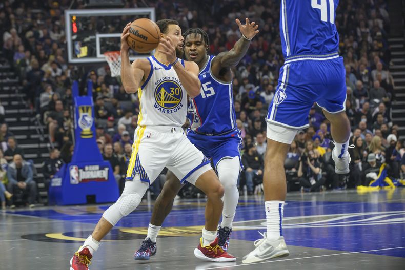 El jugador de los Warriors de Golden State Stephen Curry (30) es defendido por el jugador de los Kings de Sacramento Davion Mitchell (15) durante el primer cuarto de un juego del torneo In-Season de la NBA en Sacramento, California, el martes 28 de noviembre de 2023. (AP Foto/Randall Benton)