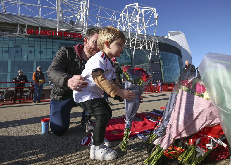 Un niño coloca flores en memoria a Bobby Charlton a los pies de la estatua The United Trinity en las afueras de Old Trafford el domingo 22 de octubre del 2023. (Barrington Coombs/PA via AP)