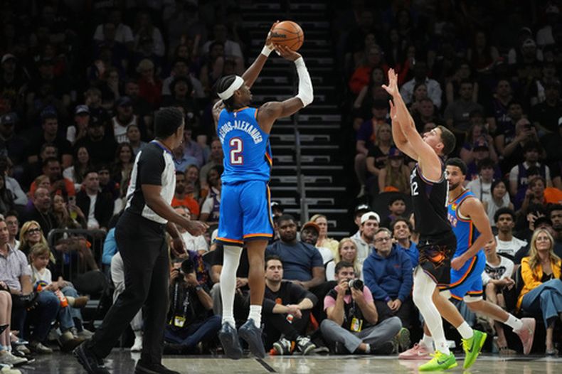 Shai Gilgeous-Alexander (2), del Thunder de Oklahoma City, dispara un triple frente a Collin Gillespie (12), de los Suns de Phoenix, durante la primera mitad del cuarto juego de la serie de primera ronda de los playoffs del baloncesto de la NBA, el lunes 27 de abril de 2026, en Phoenix. (AP Foto/Ross D. Franklin)