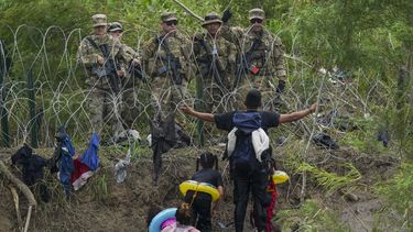 Un migrante abre los brazos frente a miembros de la Guardia Nacional de Texas ubicados detrás de alambre de púas en una de las márgenes del río Bravo, el jueves 11 de mayo de 2023, vistos desde Matamoros, México. (AP Foto/Fernando Llano)