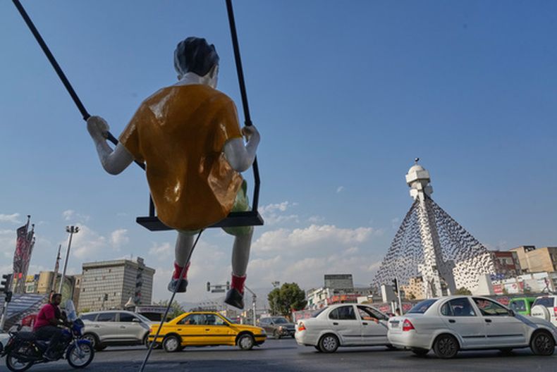 Vehículos circulan al fondo junto a una escultura de un niño columpiándose en una plaza en Teherán, Irán, el lunes 10 de agosto de 2026. (AP Foto/Vahid Salemi)