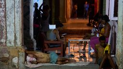 Un hombre duerme en la puerta de su casa mientras otros pasan el tiempo tratando de refrescarse en la calle en La Habana, Cuba, el martes 4 de agosto de 2026. (AP Foto/Ramón Espinosa)