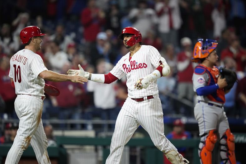 Nick Castellanos (centro) de los Filis de Filadelfia, y J.T. Realmuto (izquierda), celebran luego de rebasar al receptor venezolano de los Mets de Nueva York Francisco Álvarez, tras el jonrón de dos carreras de Castellanos en el 4to episodio. Domingo 24 de septiembre de 2023. (AP Foto/Matt Slocum)