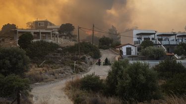 Residentes arrastran ramas de árboles mientras un incendio arde en las inmediaciones de Gennadi, en la isla de Rodas, en el sureste de Grecia, el 25 de julio de 2023. (AP Foto/Petros Giannakouris)