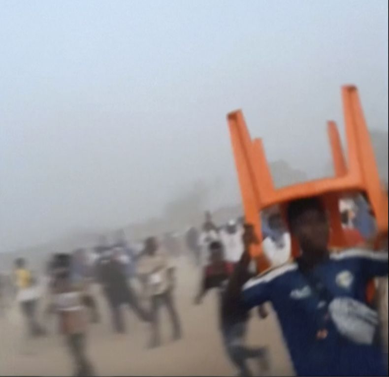 En esta imagen tomada de un video proporcionado por Nimba Sports Zaly, un hombre sostiene una silla sobre su cabeza durante una estampida en un partido de fútbol en el estadio de Nzérékoré, en Nzérékoré, Guinea, el domingo 1 de diciembre de 2024. (Nimba Sports Zaly via AP)