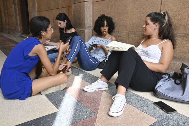 Estudiantes se sientan en un pasillo, mientras hablan y usan sus celulares en la Universidad de La Habana, Cuba, el jueves 5 de junio de 2025. (Foto AP/Jorge Luis Baños)