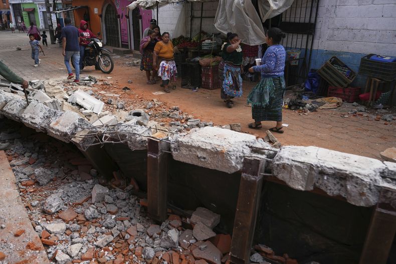 Residentes caminan el miércoles 9 de julio de 2025 junto a escombros de casas que resultaron dañadas en Santa María de Jesús, Guatemala, luego de que se registraron decenas de sismos y réplicas en cuestión de horas. (AP Foto/Moisés Castillo)